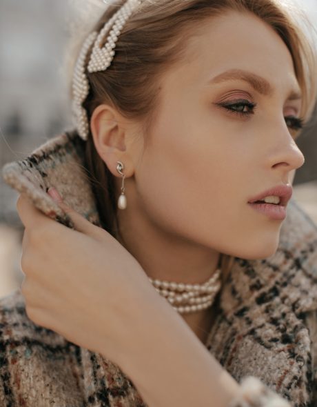 Close-up portrait of blonde young pretty woman in pearl jewelry and checkered tweed coat posing outdoors.